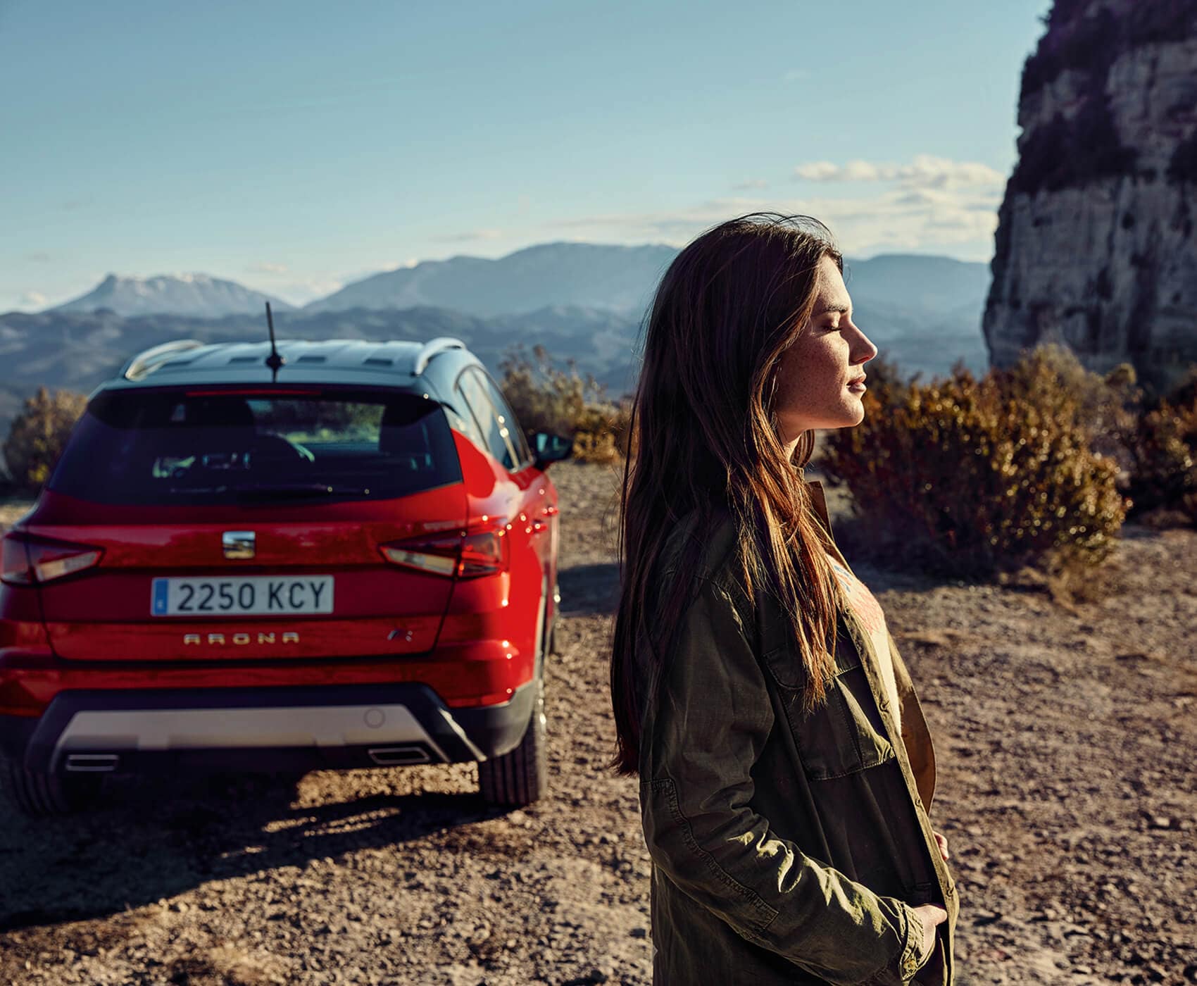 SEAT new car services – rear view of SEAT Arona crossover SUV parked in a dessert with a profile view of a woman